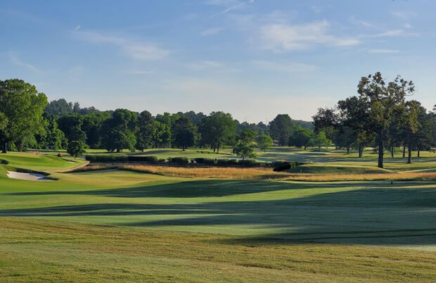 Scenic golf course fairway with bunkers, pond, and trees on a sunny morning.