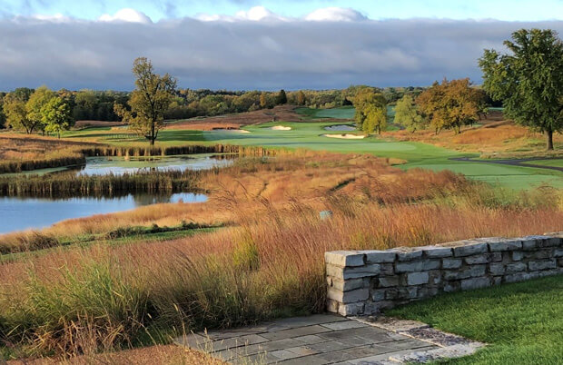 Scenic golf course with rolling fairways, ponds, bunkers, and autumn trees under cloudy sky