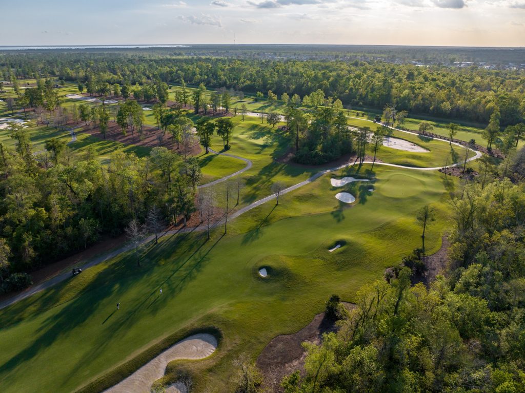 Aerial view of a lush, tree-lined golf course with fairways, sand bunkers, and winding cart paths