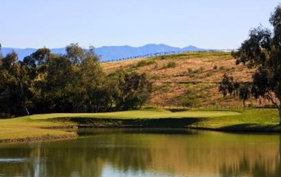 Scenic golf course green beside a lake with rolling hills and mountain backdrop