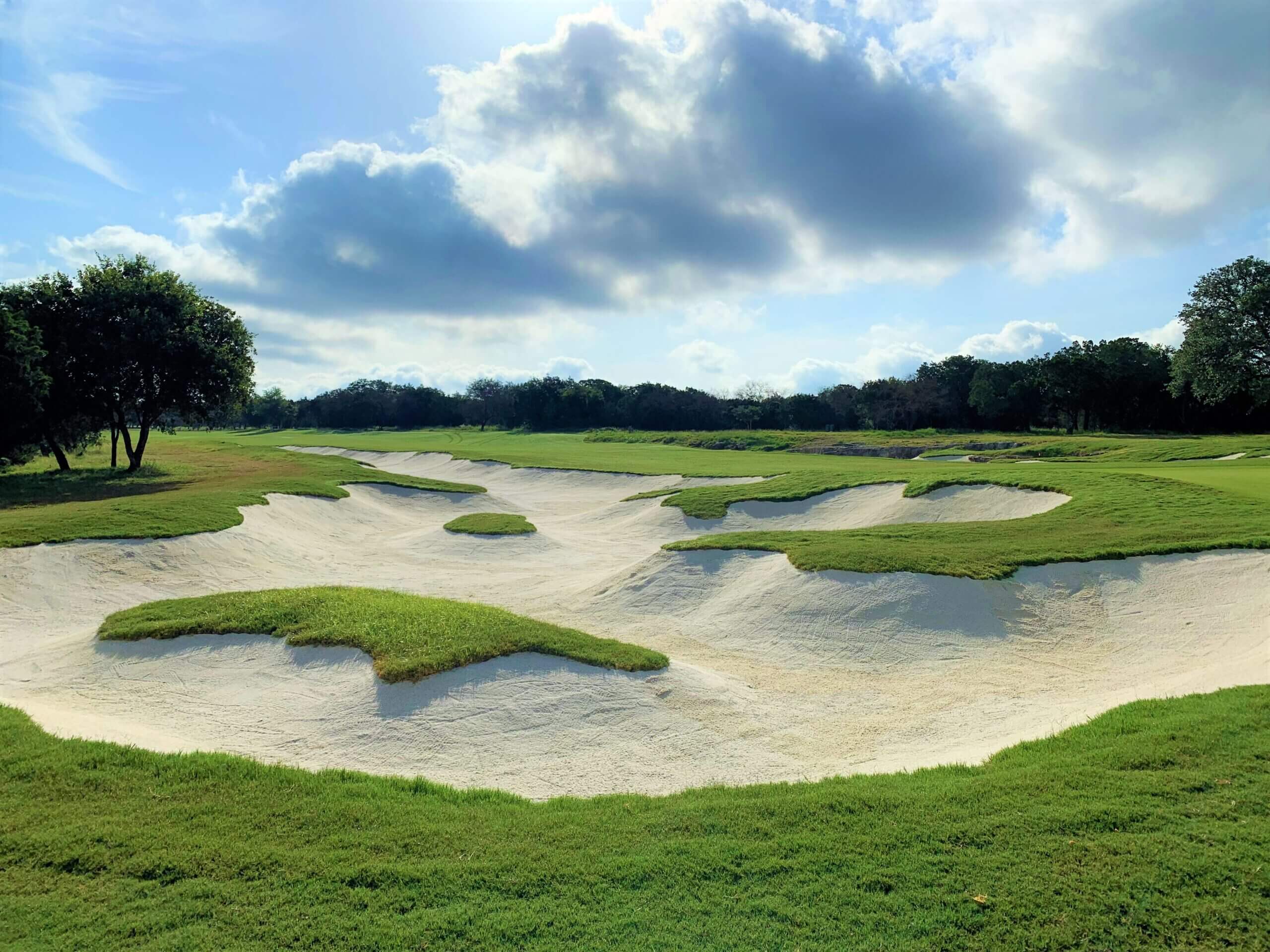 Championship golf course fairway with dramatic sand bunkers under blue sky